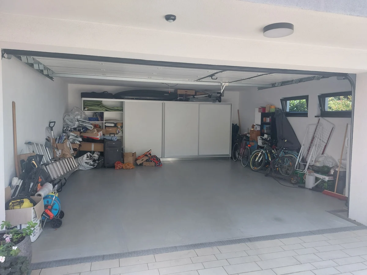 A garage with boxes, ladders and bikes piled along the walls, before the space was organized