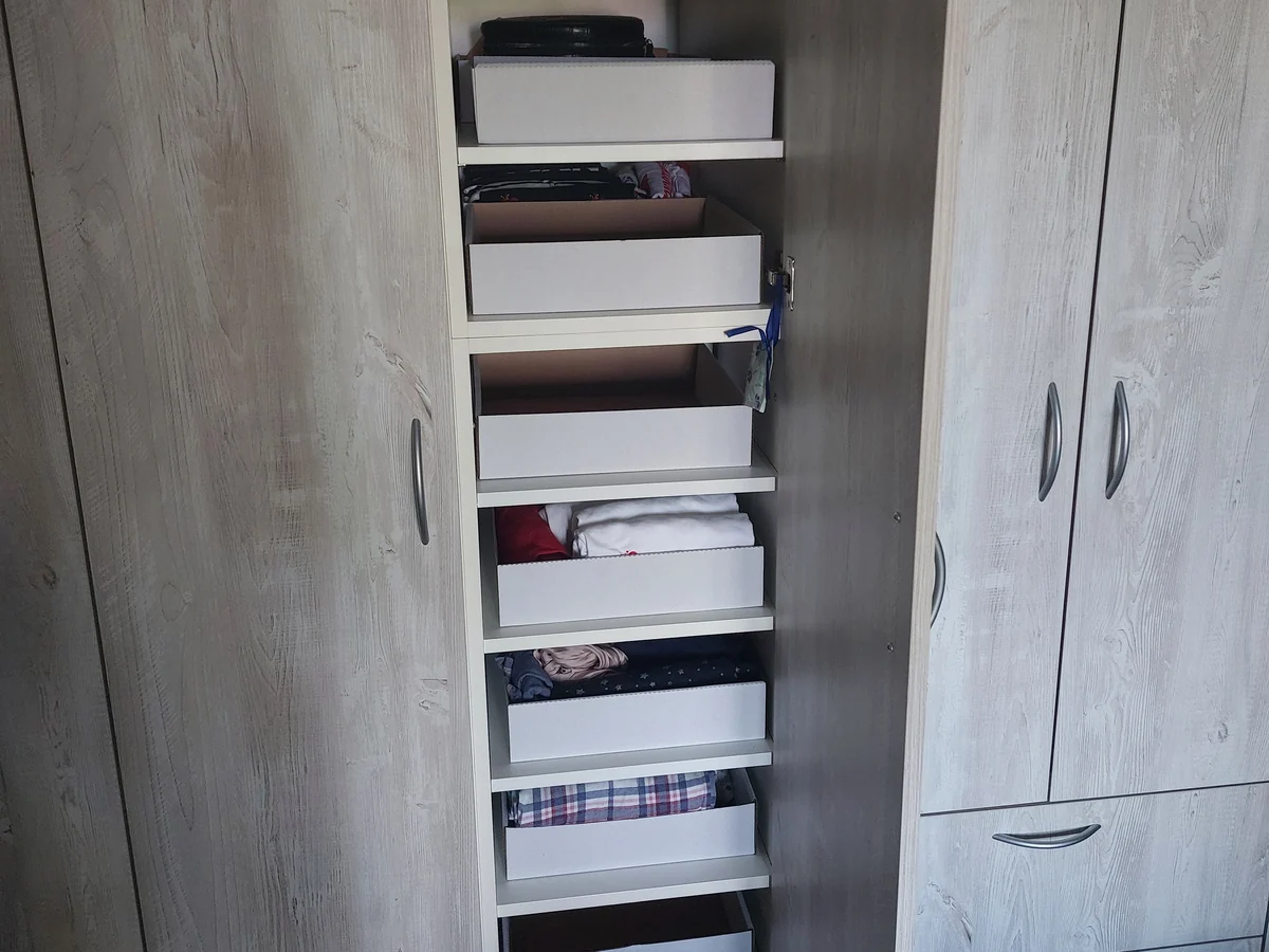 The same wardrobe after organizing — storage boxes and folded clothes on every shelf