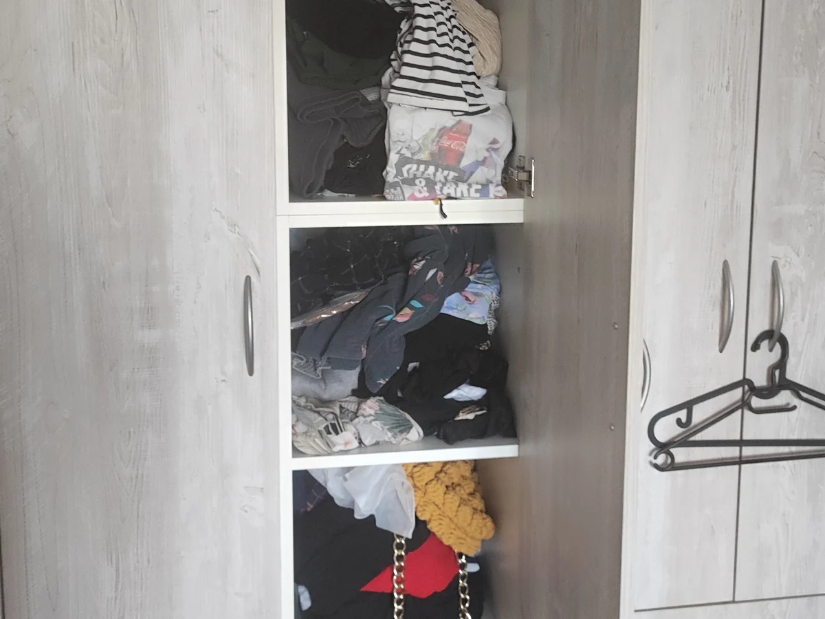 A tall wardrobe with shelves full of unfolded clothes, before the space was organized
