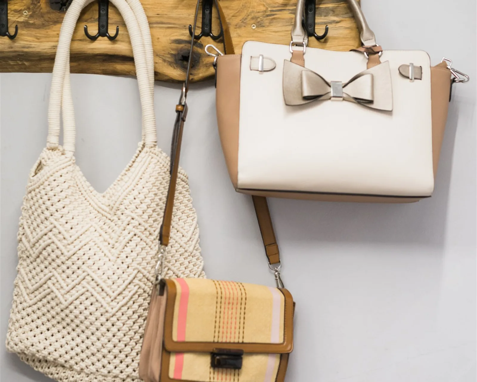 A crochet tote, a white bag with a bow and a small shoulder bag hanging on a wooden rack — organizing bags the KonMari® way