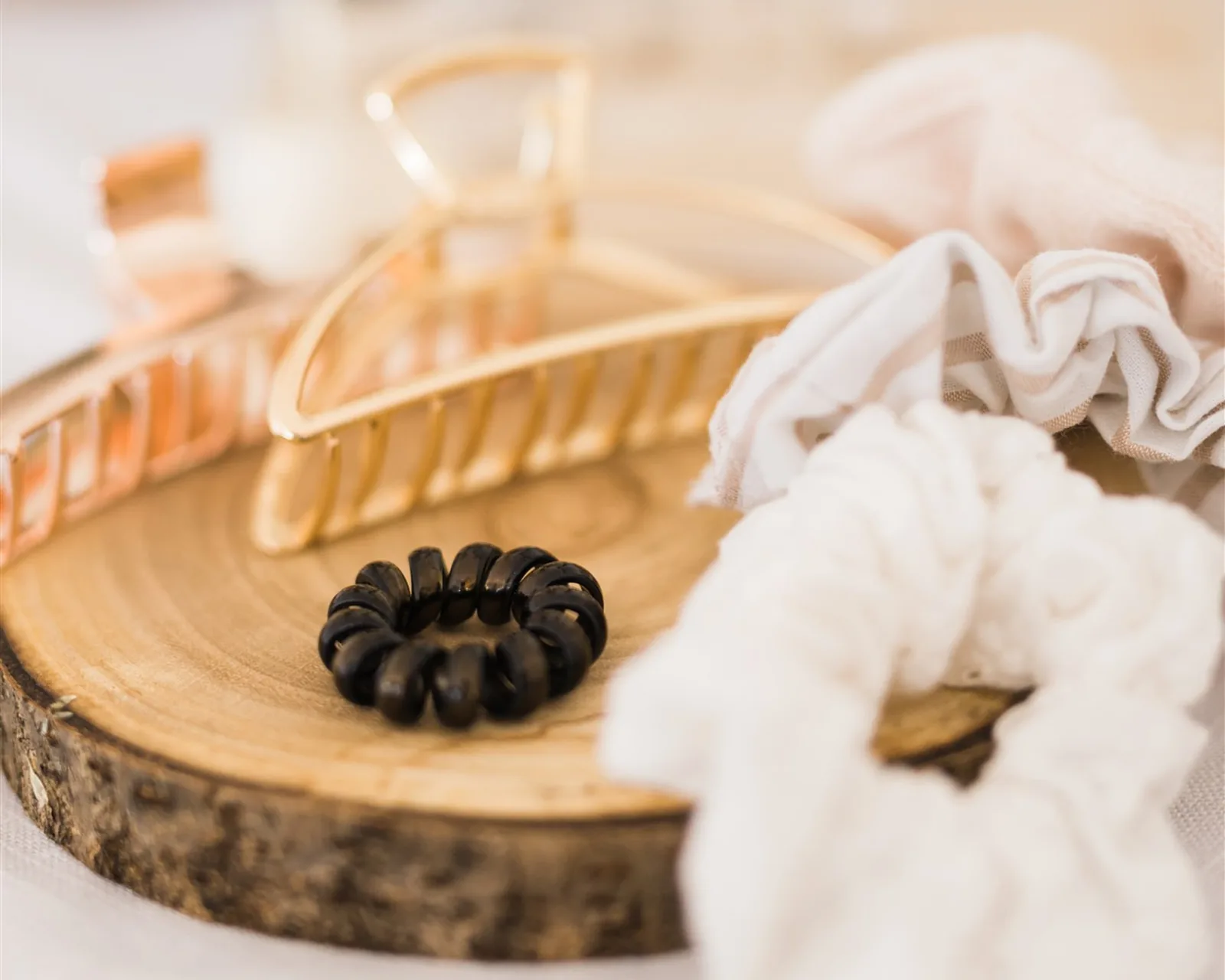 A gold hair clip, scrunchies and hair ties on a wooden tray — organizing hair accessories and jewellery the KonMari® way