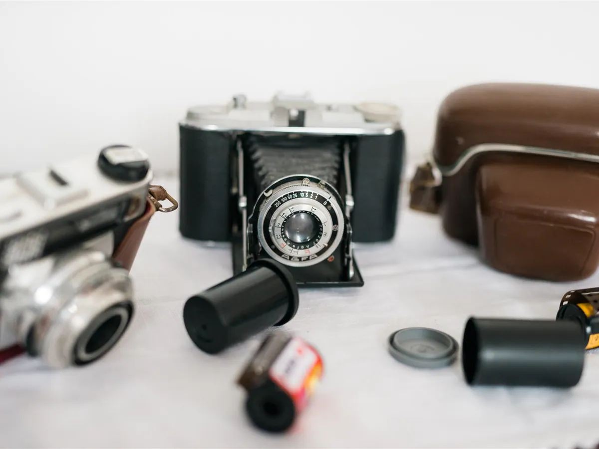 Vintage cameras with a leather case and rolls of film on a white surface