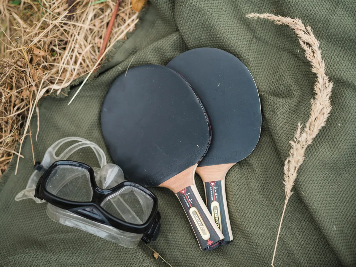 Table tennis bats and a diving mask on a green blanket in the grass