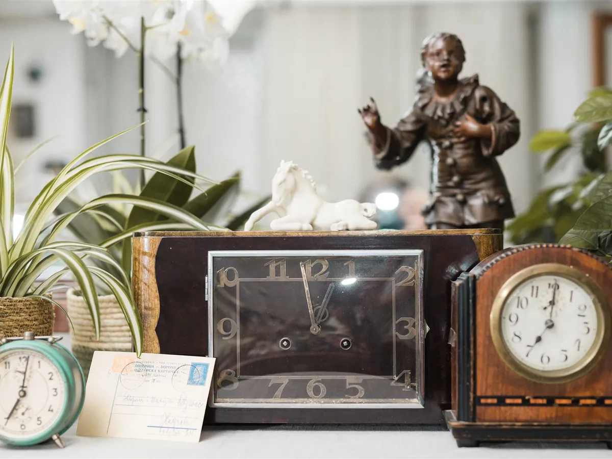 Three antique clocks, a postcard and a porcelain horse among plants