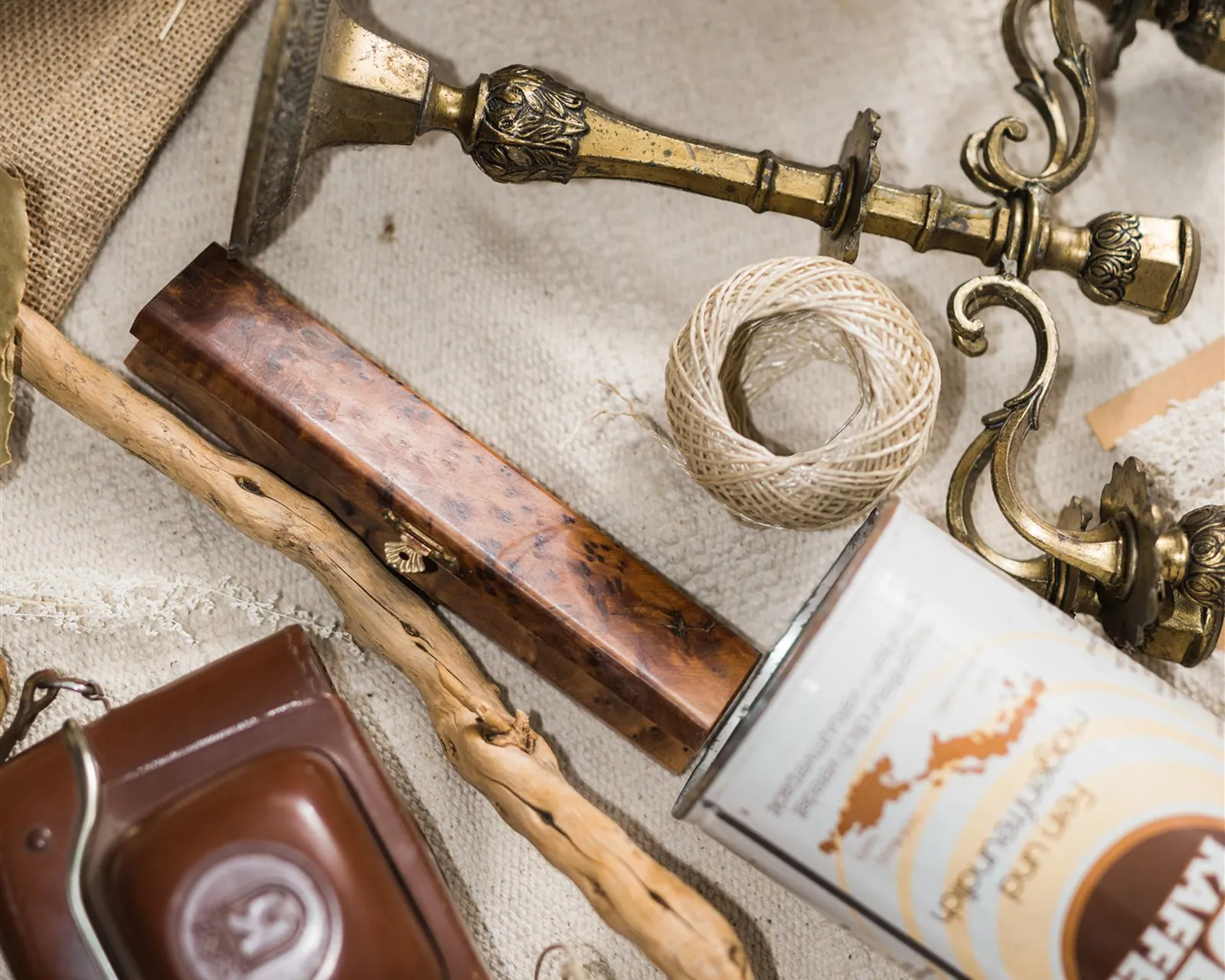 Miscellaneous objects on linen: an antique candelabra, a camera, twine, cinnamon bark and lace