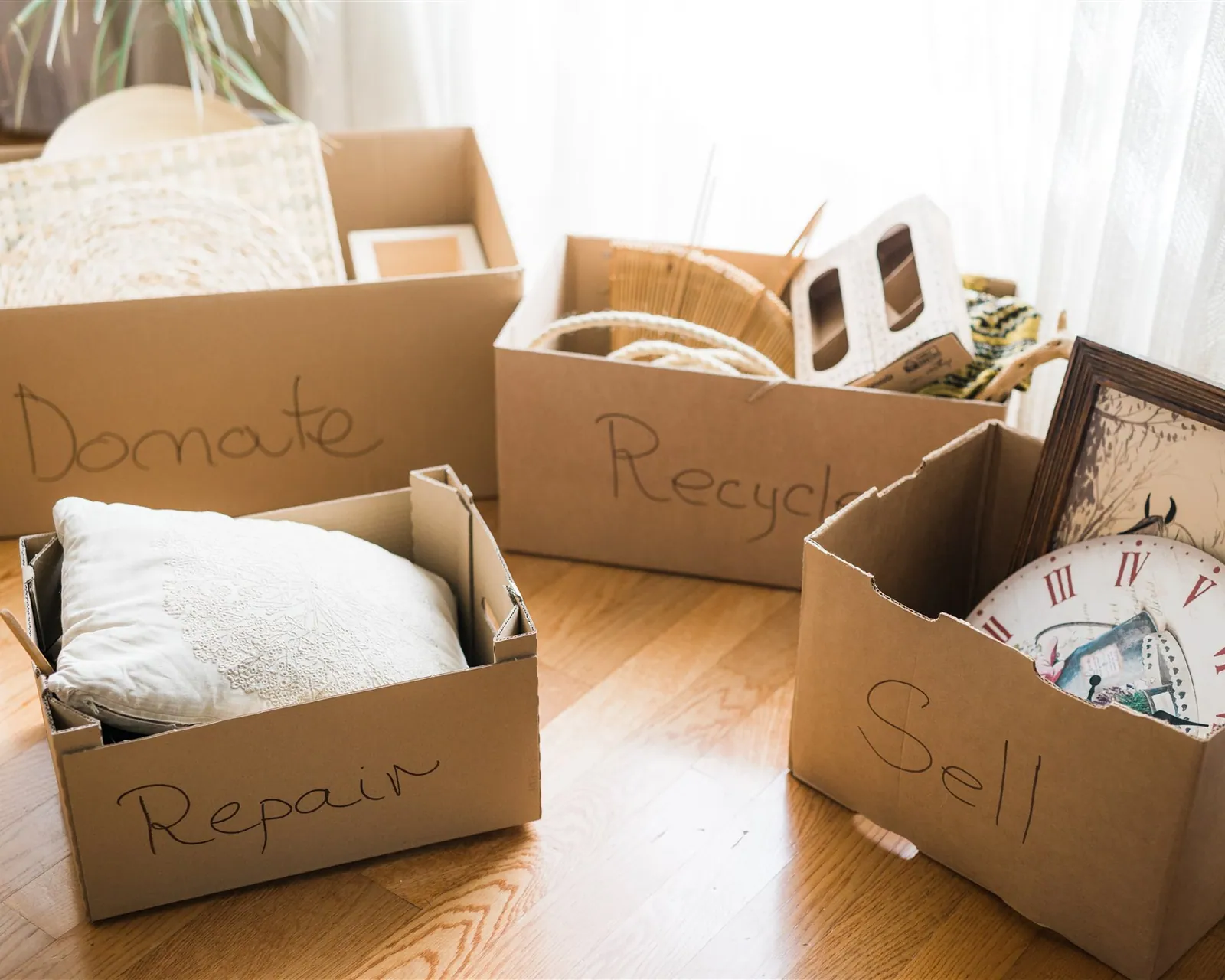 Four cardboard boxes labelled Donate, Recycle, Repair and Sell on a wooden floor