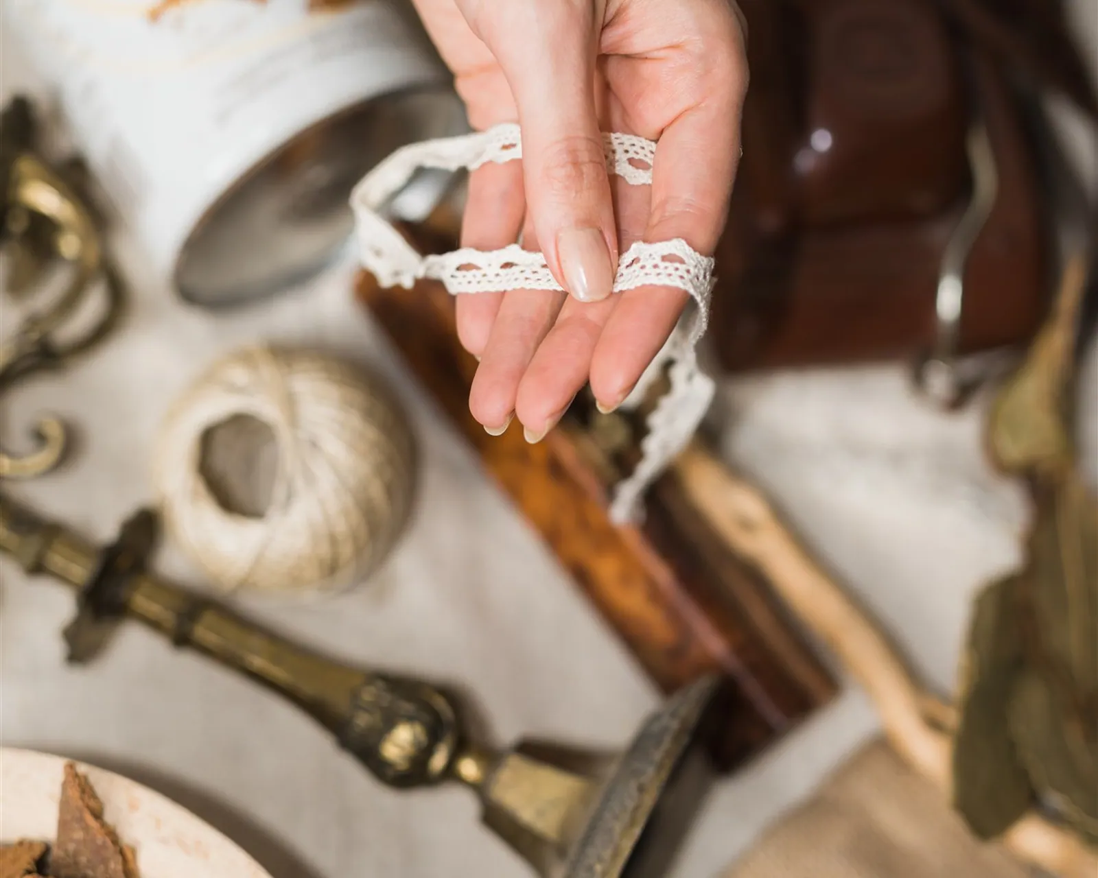 A hand holding a lace ribbon above objects laid out on linen — the joy check in the komono category