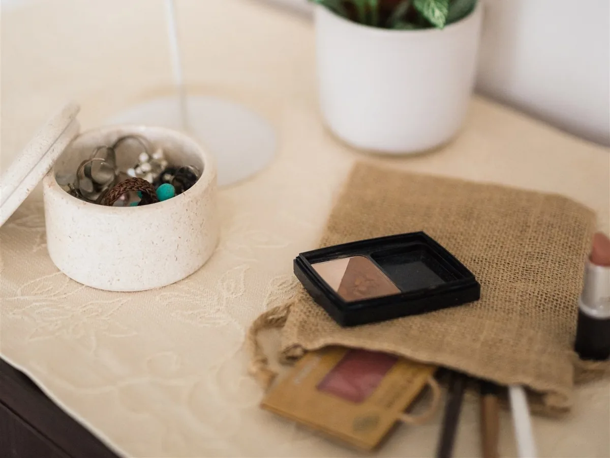 A jewellery dish, an eyeshadow palette and a lipstick on a dresser beside a potted plant