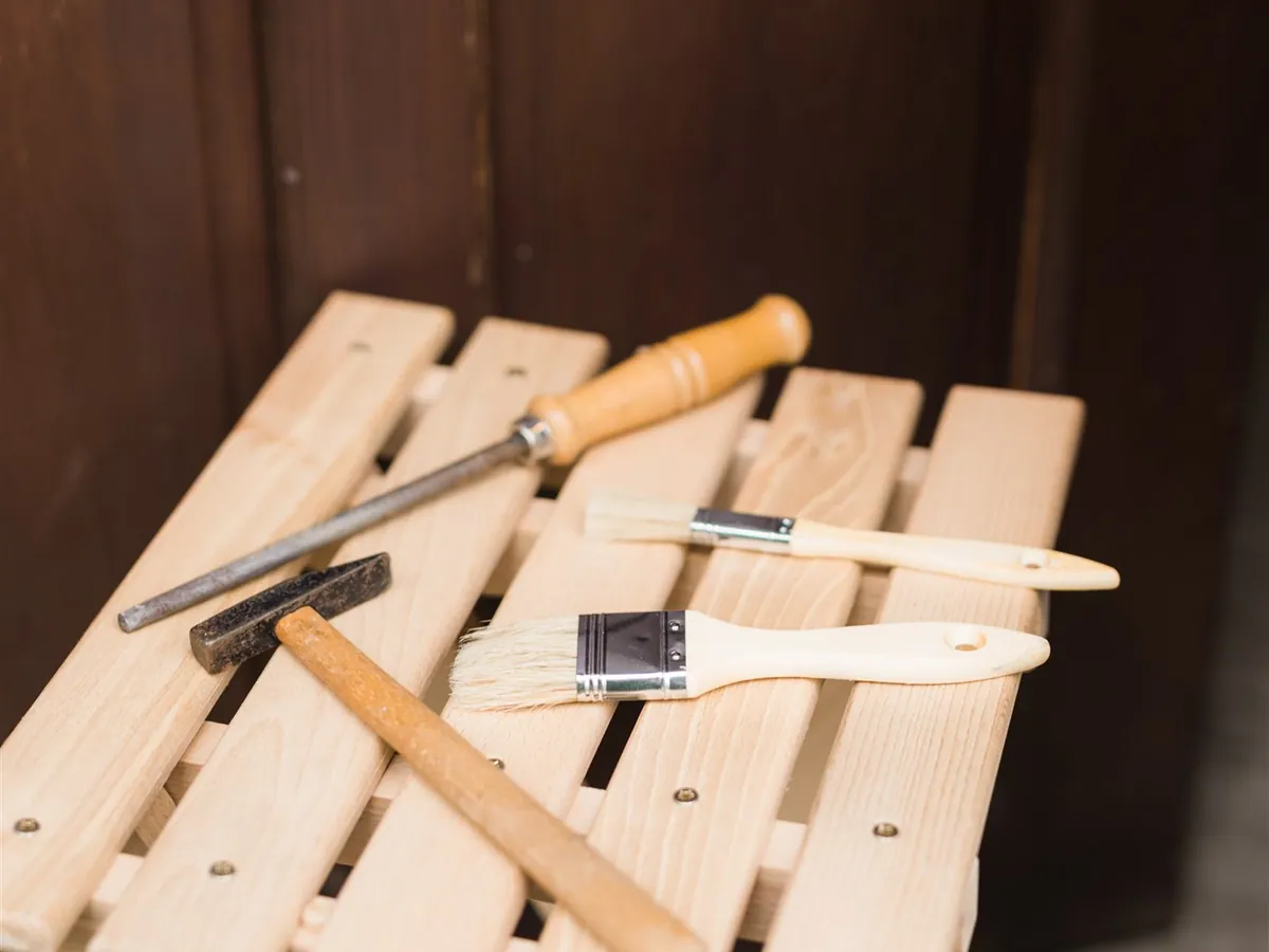 A hammer, a chisel and brushes on a small wooden stool in front of a dark door