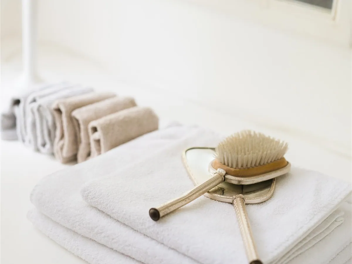 White towels folded on a dresser beside an antique silver brush and mirror
