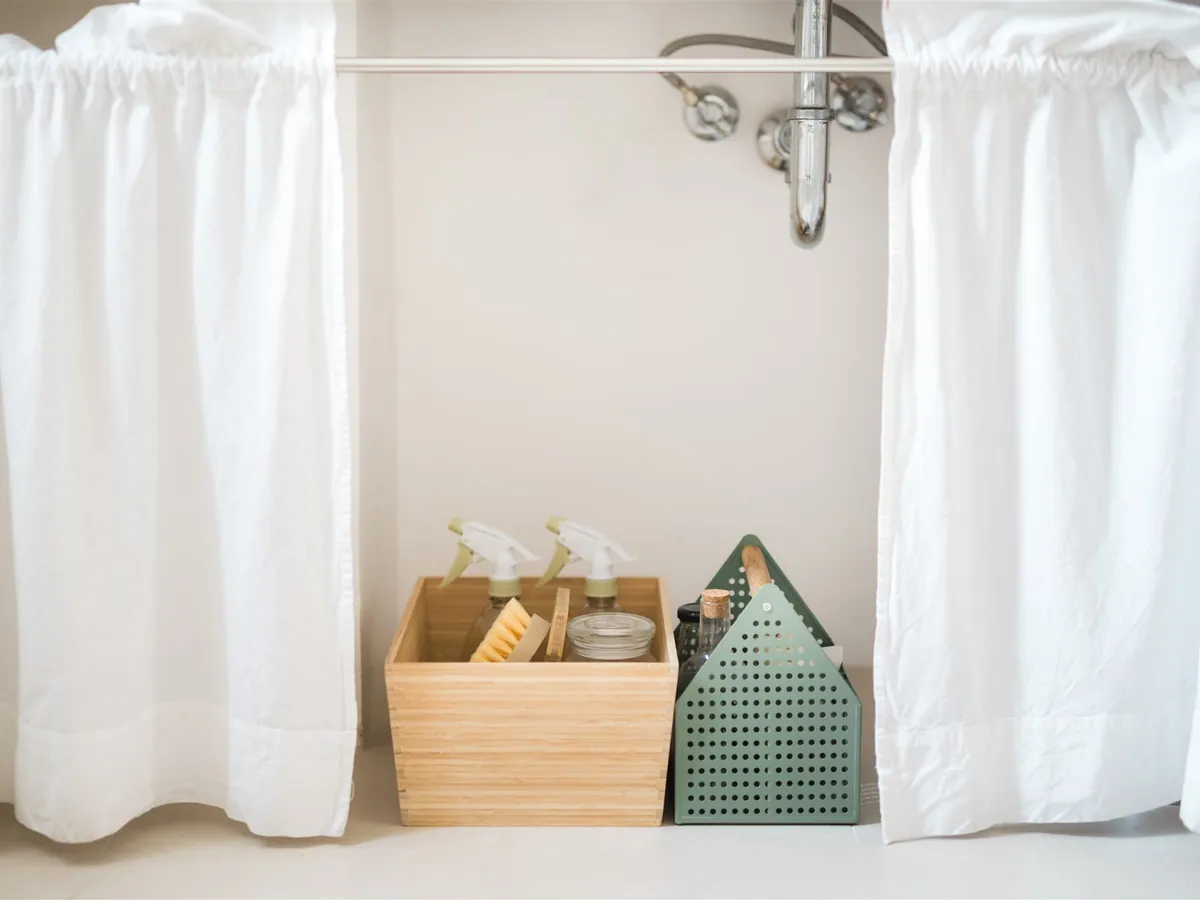 A wooden box of natural cleaning supplies and a brush under a sink