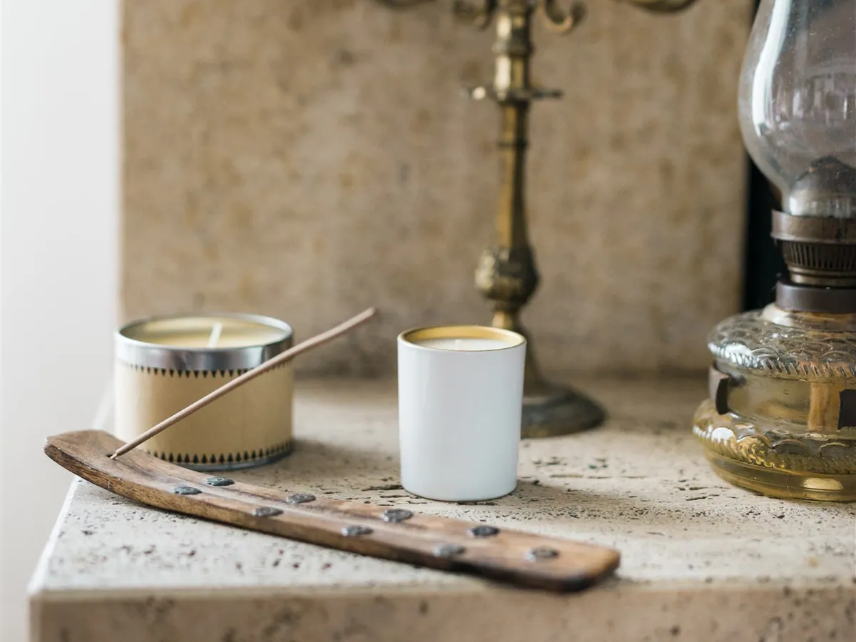 Candles, an incense stick, an antique candelabra and an oil lamp on a stone shelf