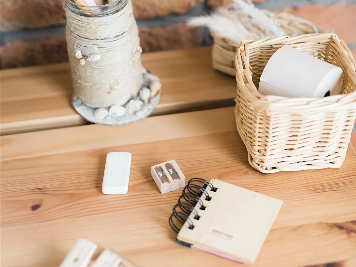 Pencils in a twine-wrapped jar, rulers, an eraser and a small notebook on a wooden desk