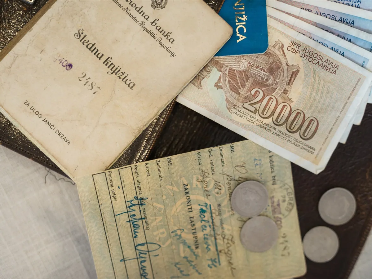 An old savings book, Yugoslav banknotes and coins on a leather folder