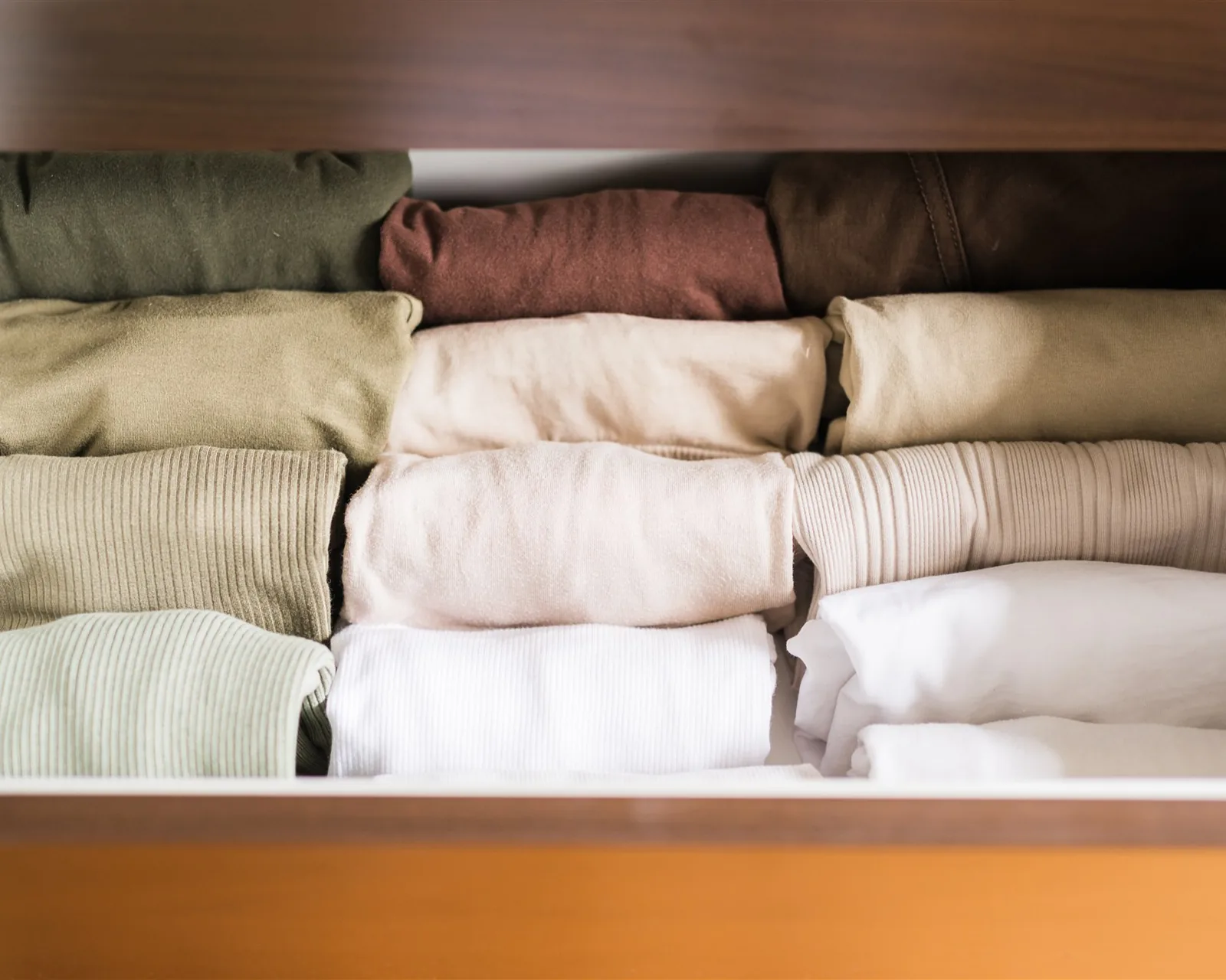 T-shirts and jumpers folded upright in a wooden drawer — clothes, the first KonMari® category