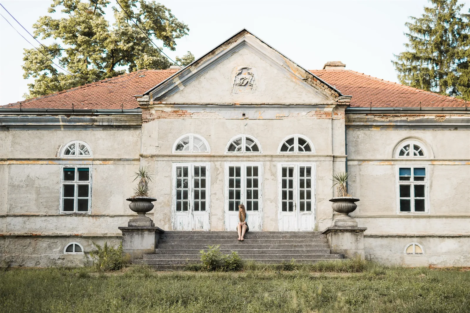 A woman sitting on the steps of an old house surrounded by grass and trees — imagining your ideal lifestyle in the KonMari® method