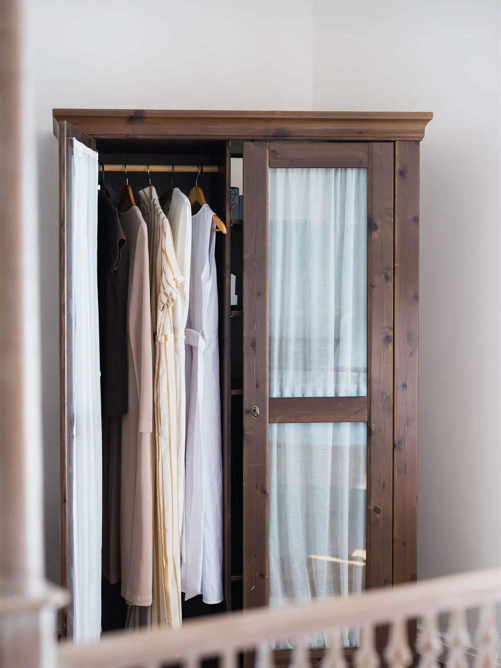 Clothes hanging in a wooden wardrobe, arranged from darker to lighter — organizing a closet the KonMari way
