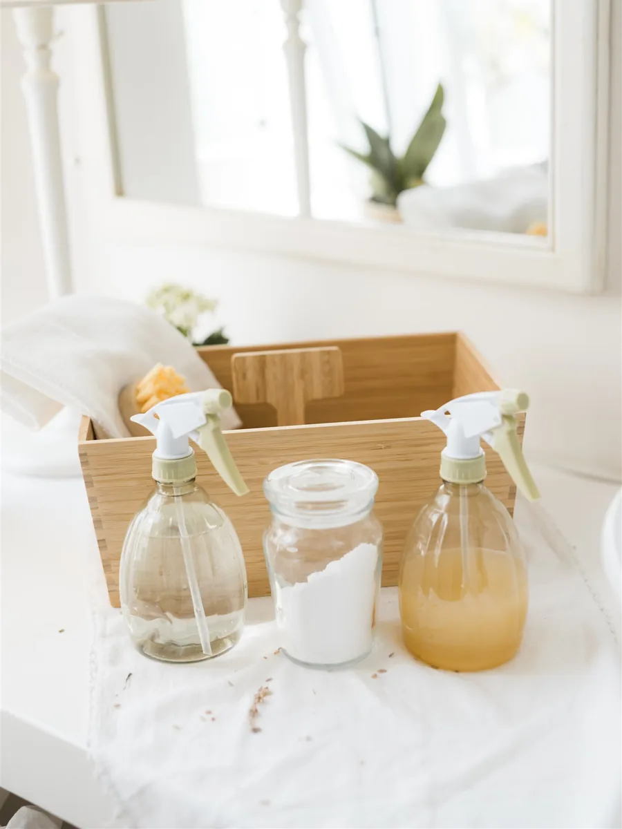 Two glass spray bottles and a jar of baking soda in a bamboo box