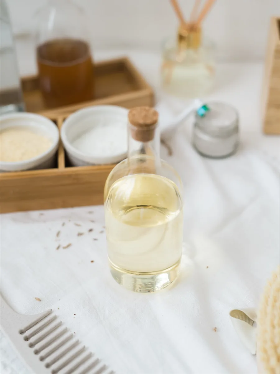 A glass bottle of oil and small bowls of ingredients for a makeup-removing emulsion