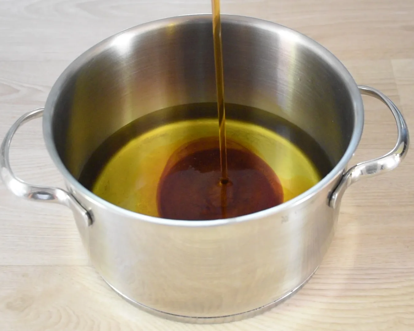 A darker oil being poured into a pot that already holds olive oil