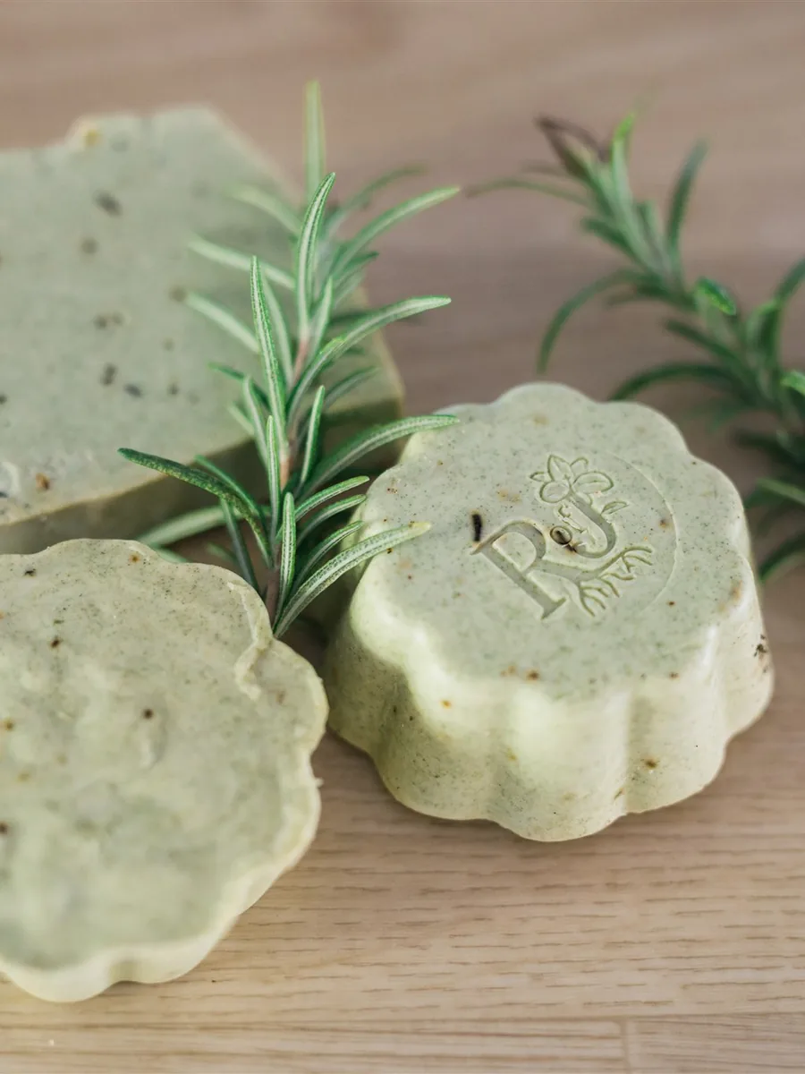 Green rosemary soaps stamped with the Root of Joy mark beside sprigs of rosemary
